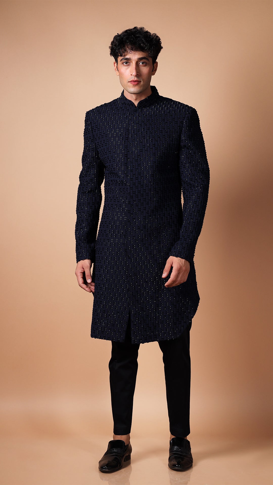 The model strikes a dynamic pose, bringing movement to the Cut Dana Bluish Black Full Embroidered IndoWestern. The full-length shot captures the outfit's versatility and stylish appeal. The embroidery glistens under the studio lights, making the ensemble perfect for grooms and special occasions.