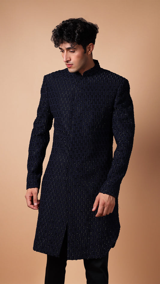 The model is captured in a full side view, highlighting the sleek silhouette of the IndoWestern outfit. The embroidery detail runs along the side, emphasizing the craftsmanship and the luxurious texture of the fabric. The model's posture enhances the elegance of the ensemble.