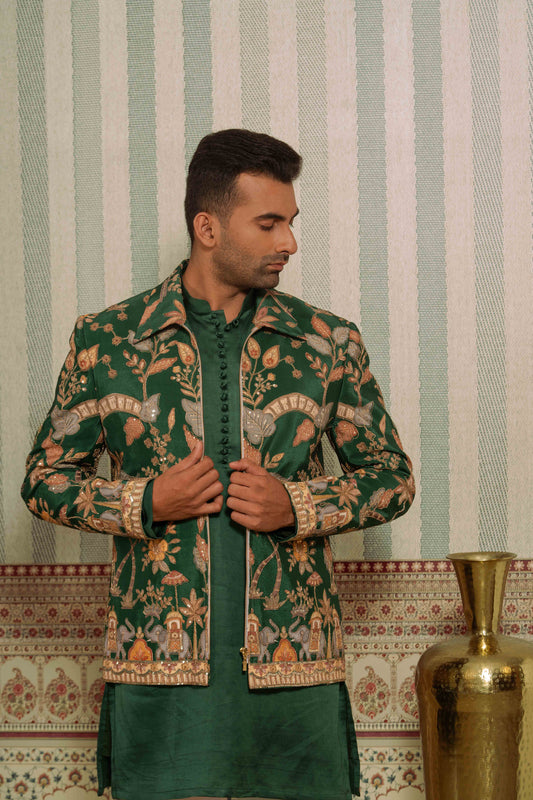 A man wearing a green bomber jacket with a detailed gold and beige embroidered jacket, standing in front of a green and white striped wall.
