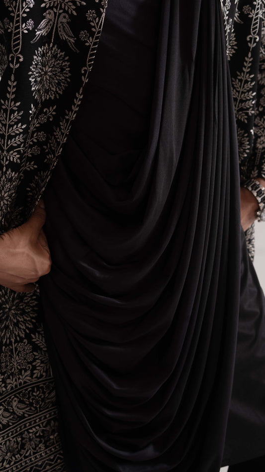 A close-up of a draped black indowestern with a satin-like sheen, layered over a black embroidered outer layer with silver floral detailing.
