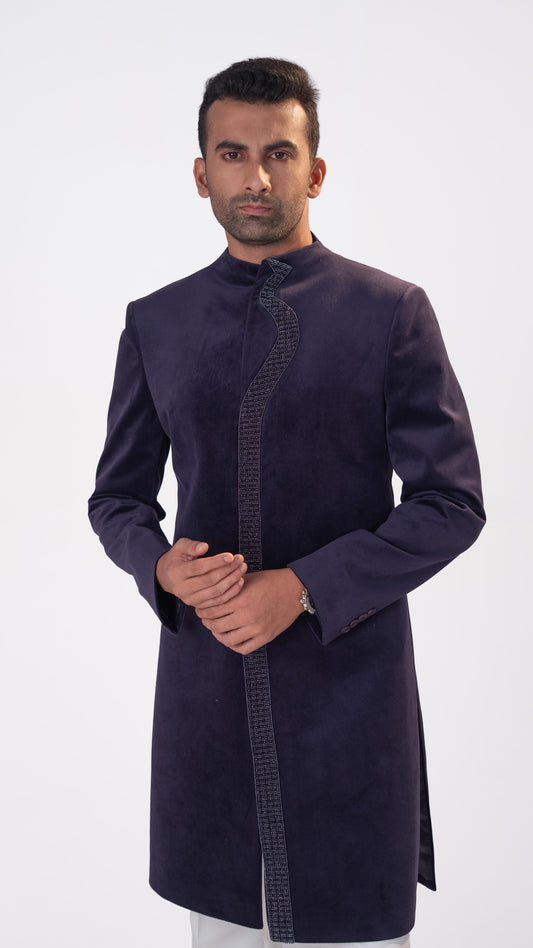 A man wearing a purple indowestern with a textured patterned trim down the front, standing against a plain light gray background.