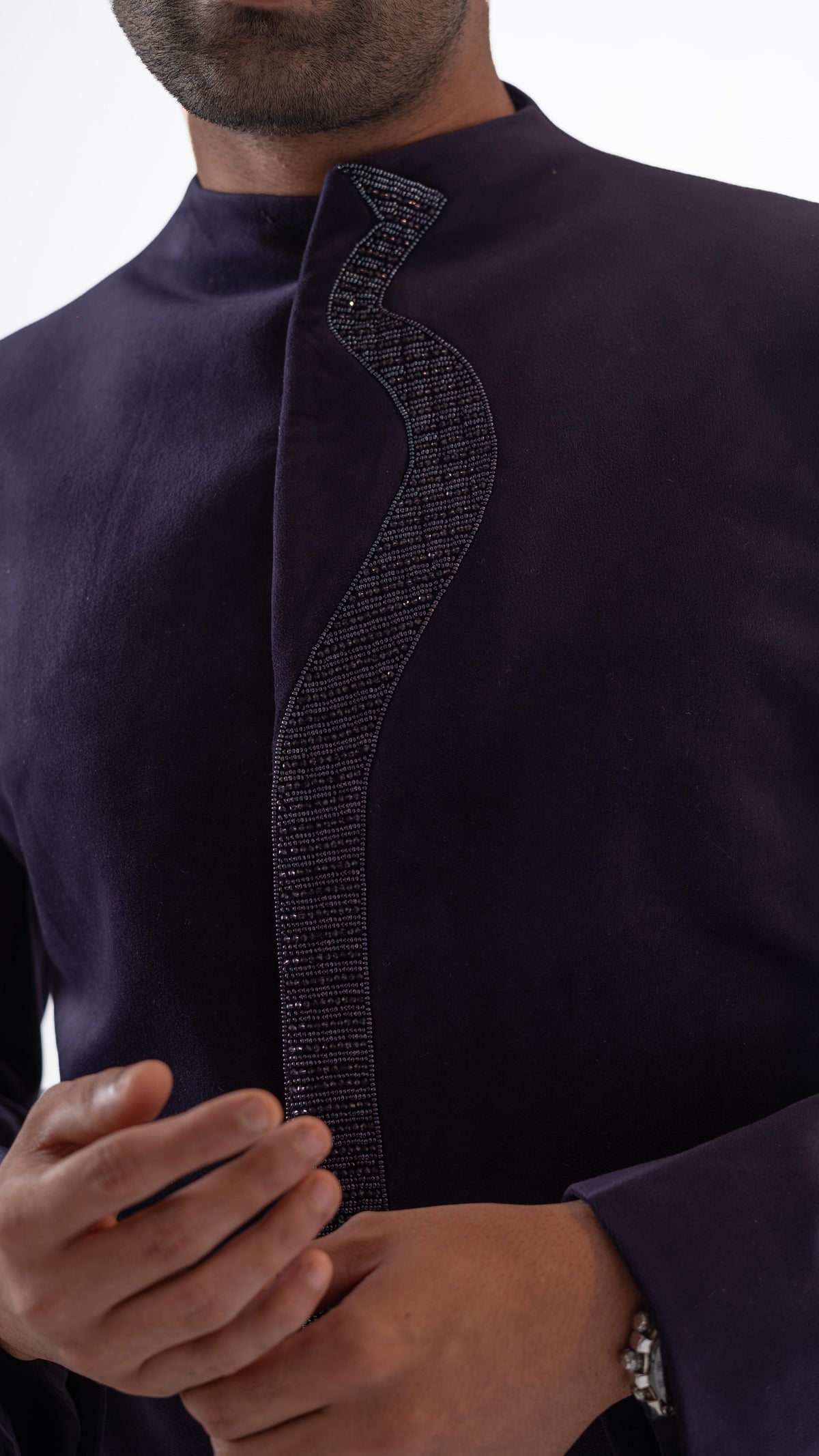 Close-up of a man wearing a dark purple traditional indowestern with a textured, beaded asymmetrical front panel and a high collar.