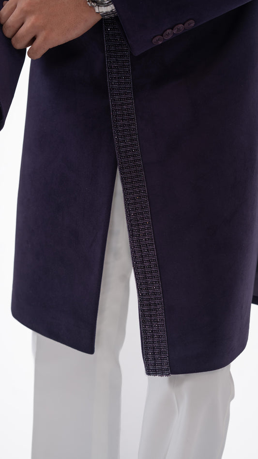 Close-up of a purple indowestern worn with white trousers, showing a textured vertical trim and part of a person's hand and wrist.