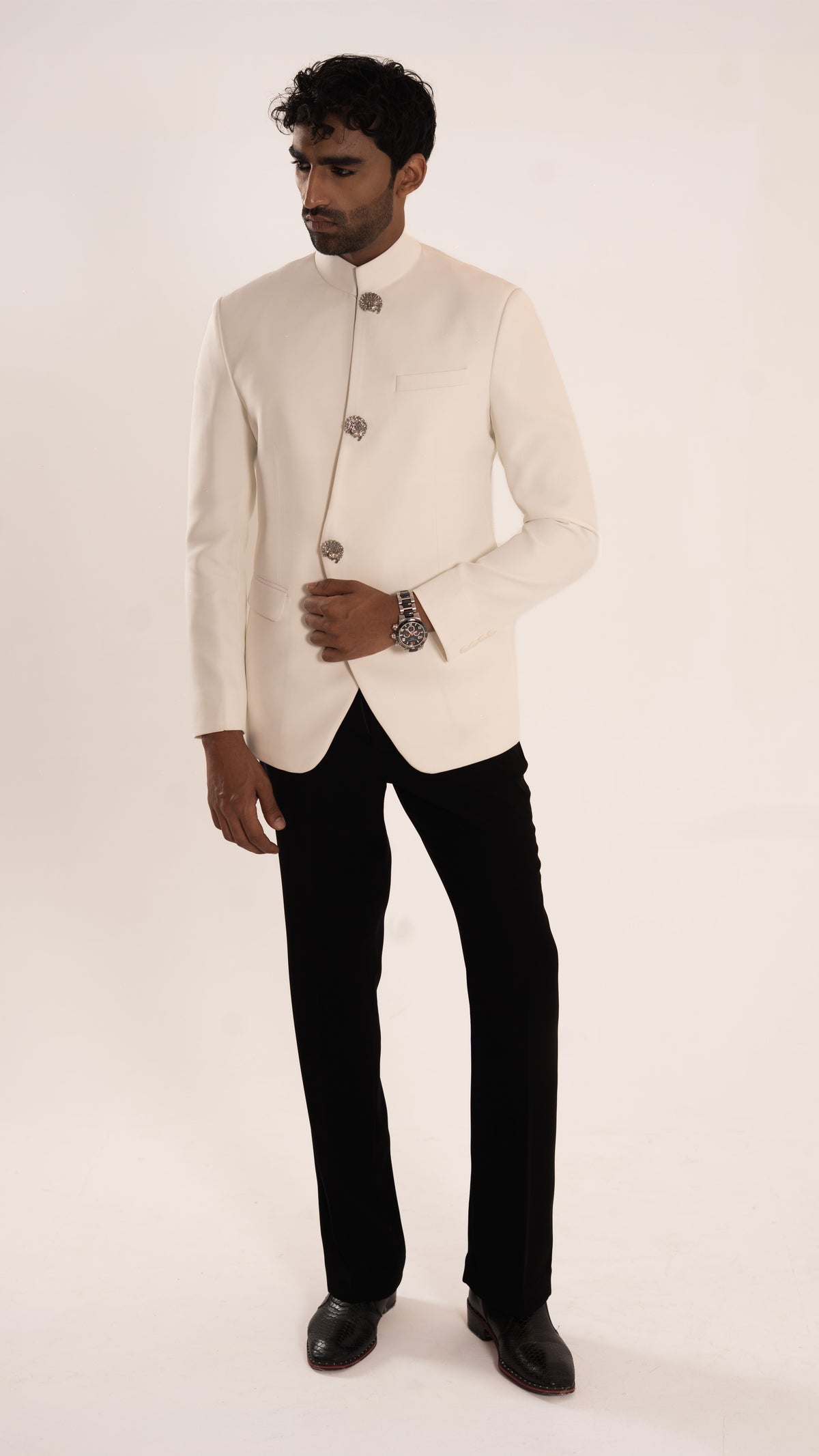 A man modeling a off-white Indian ethnic jacket (bandhgala) paired with black trousers and black shoes, standing against a plain off-white studio background.