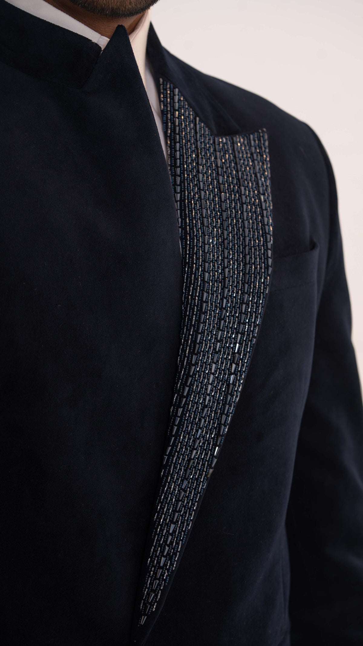 Close-up of a dark navy velvet blazer with a textured, beaded silver and black vertical panel on the lapel, worn over a white collared shirt.