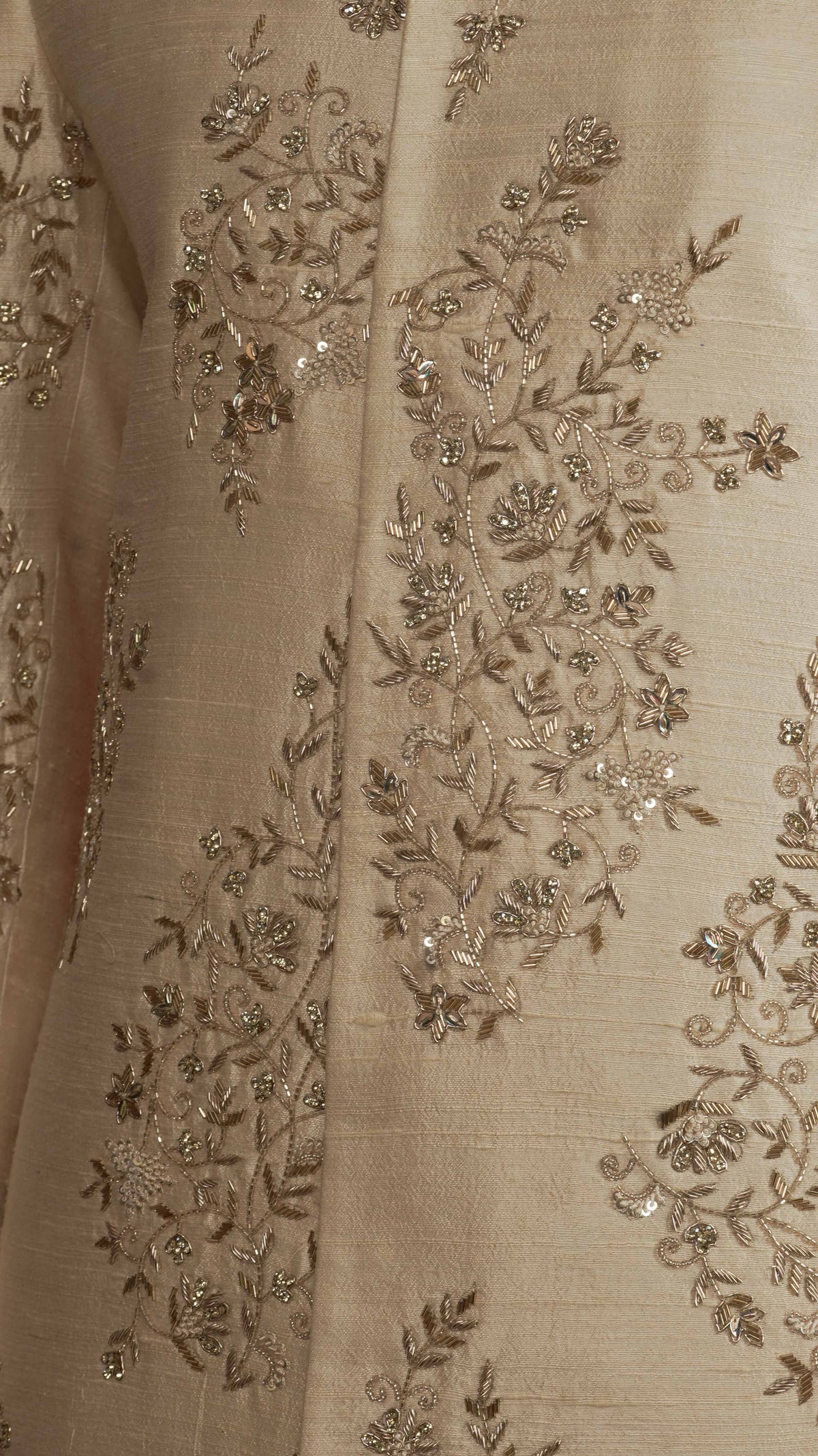 Close-up of a light rose gold fabric garment with intricate metallic gold floral embroidery and sequin embellishments.