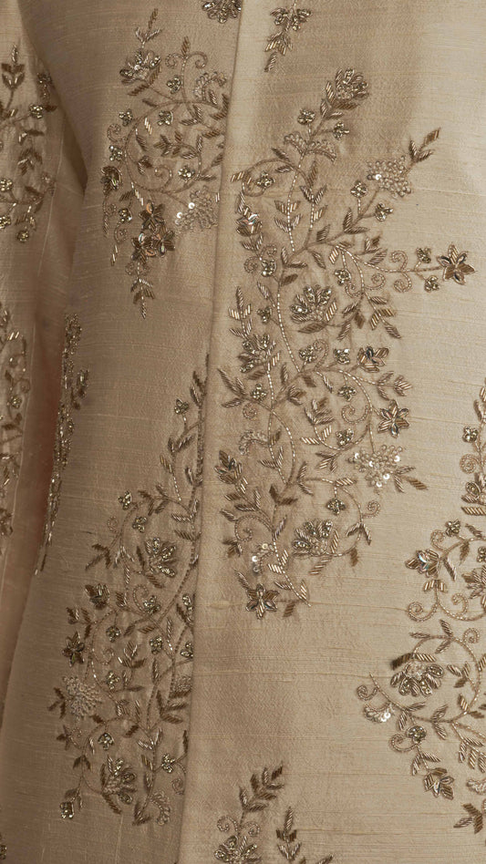 Close-up of a light rose gold fabric garment with intricate metallic gold floral embroidery and sequin embellishments.