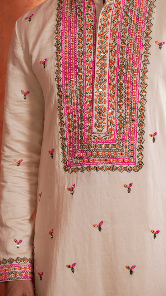 A close-up of a cream-colored traditional kurta featuring intricate multicolor embroidery around the V-neckline and scattered small floral motifs on the fabric.