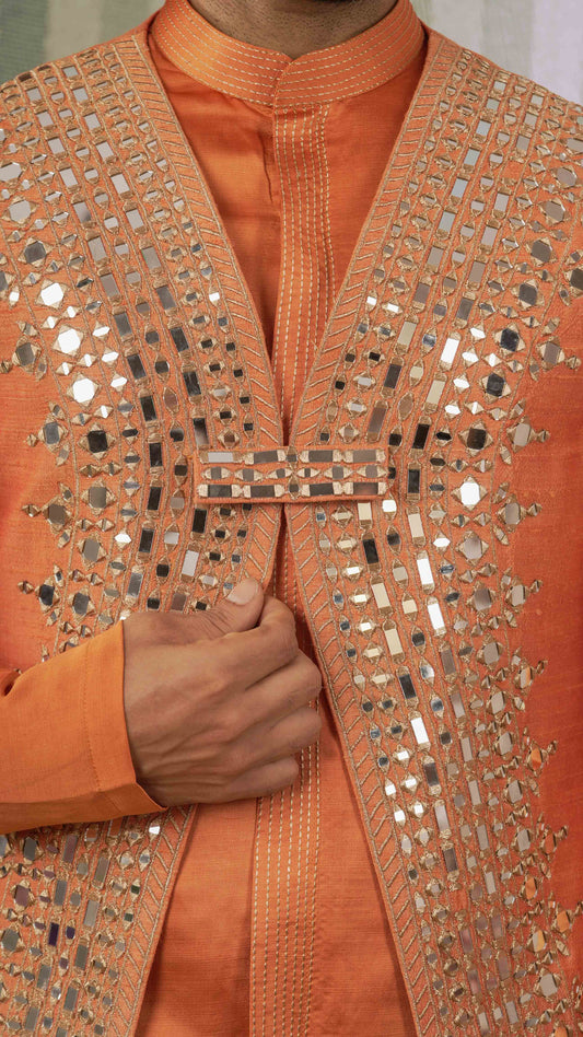 Close-up of a person wearing an orange kurta with extensive silver mirror work and metallic embellishments on the front panel and lapels.