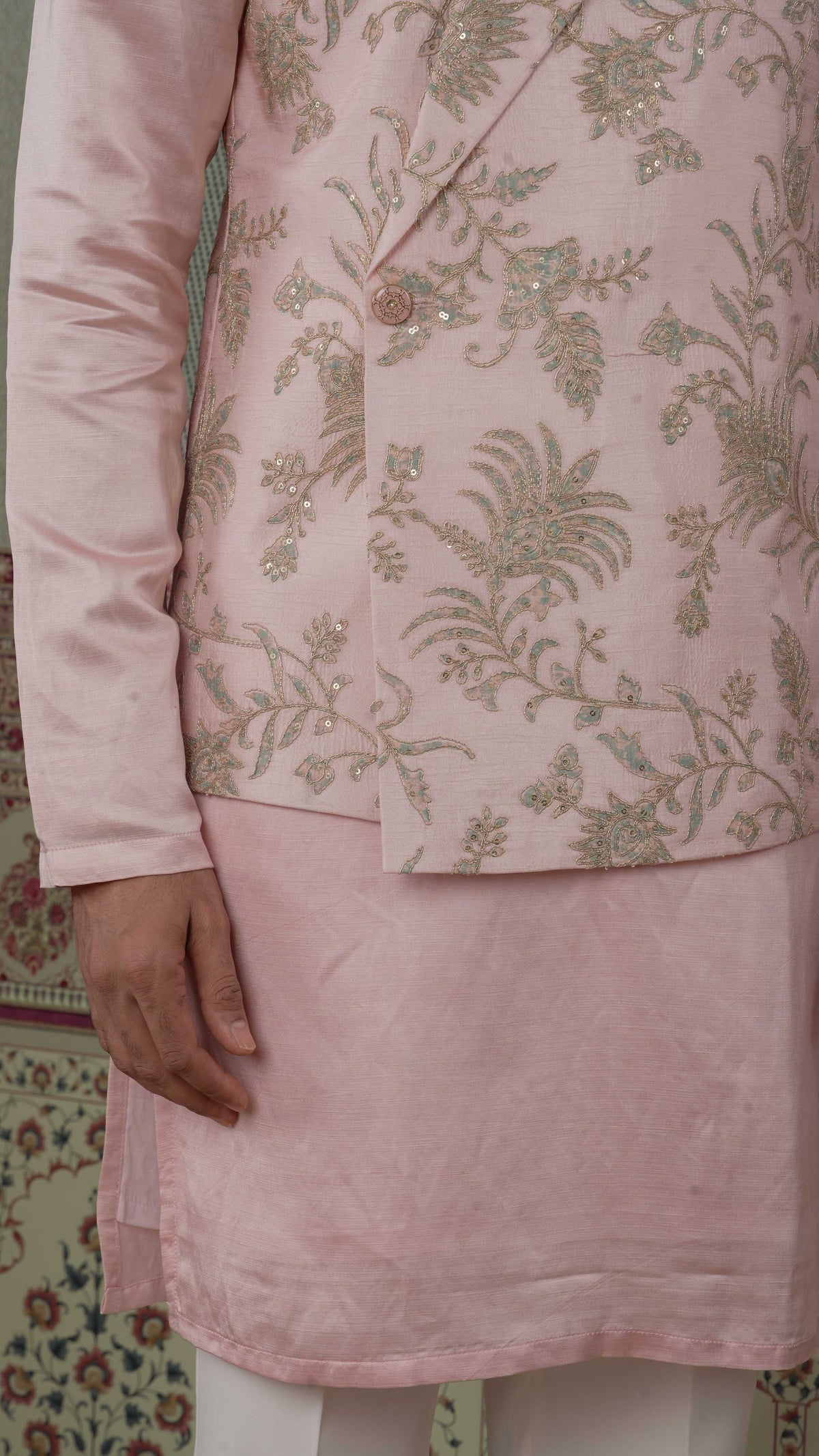 A close-up of a light pink bundi kurta outfit featuring a heavily embroidered blazer with gold and bluish floral patterns and a solid pink kurta.