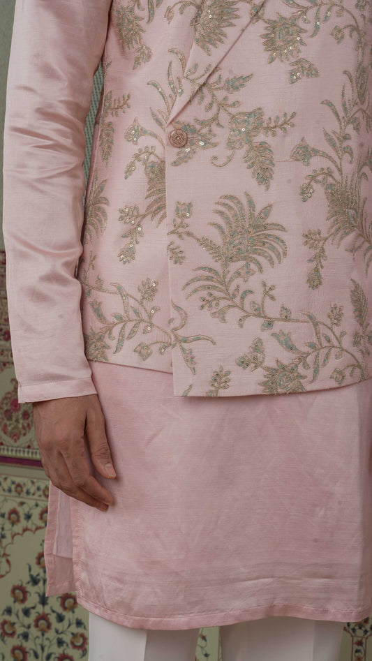 A close-up of a light pink bundi kurta outfit featuring a heavily embroidered blazer with gold and bluish floral patterns and a solid pink kurta.