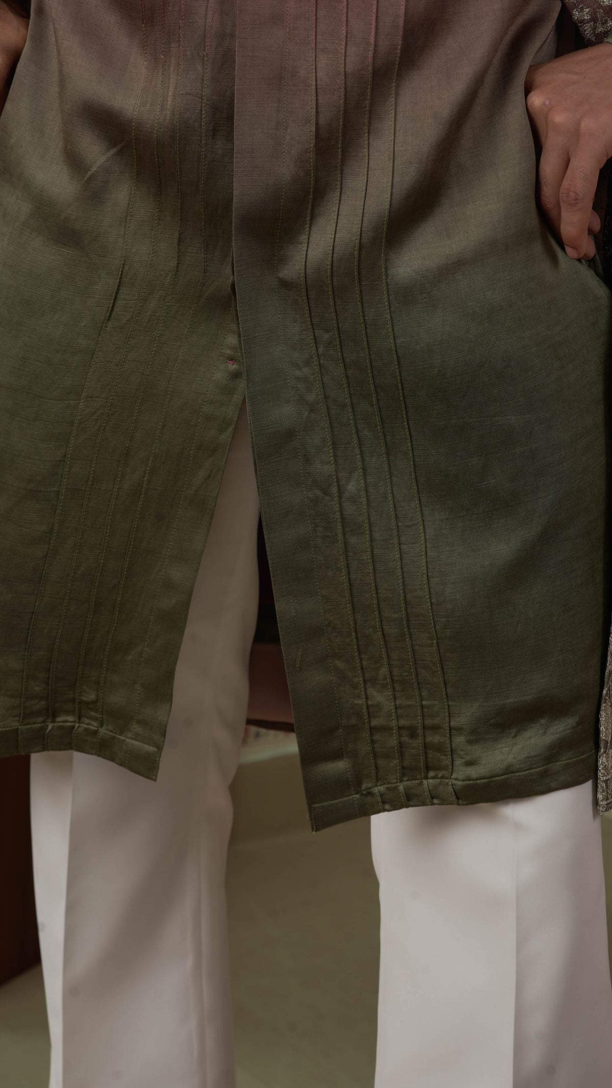 Close-up of a person wearing an olive green orange kurta with vertical pleats, paired with white trousers.