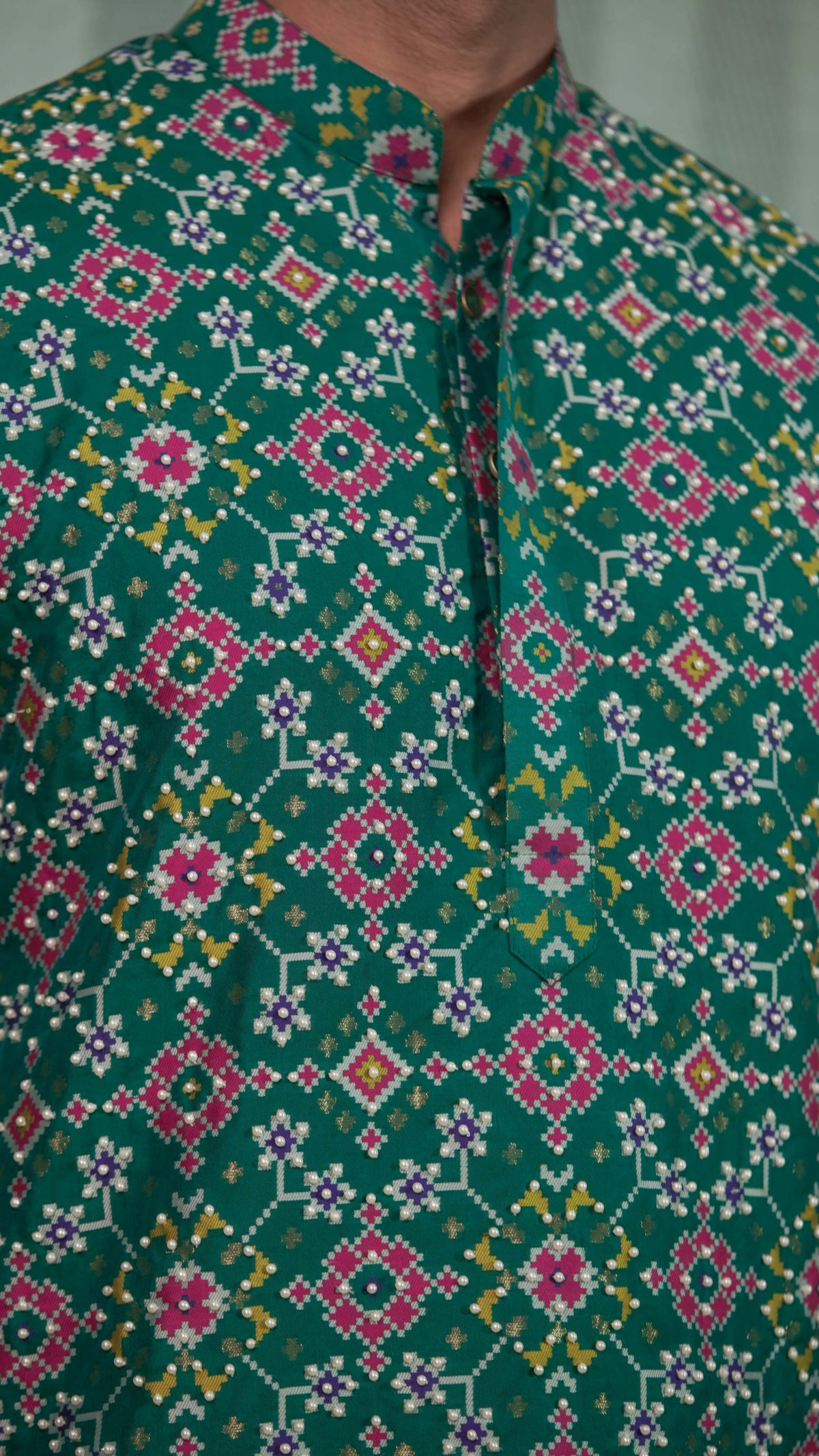 Close-up of a green hand embroidered kurta or shirt with a mandarin collar and button placket, featuring intricate pink, white, and yellow geometric and floral patterns.