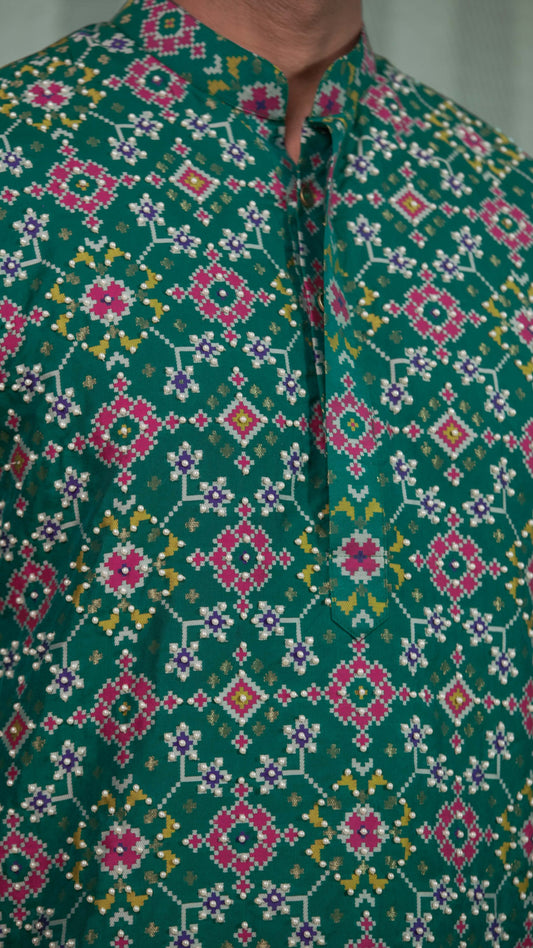 Close-up of a green hand embroidered kurta or shirt with a mandarin collar and button placket, featuring intricate pink, white, and yellow geometric and floral patterns.