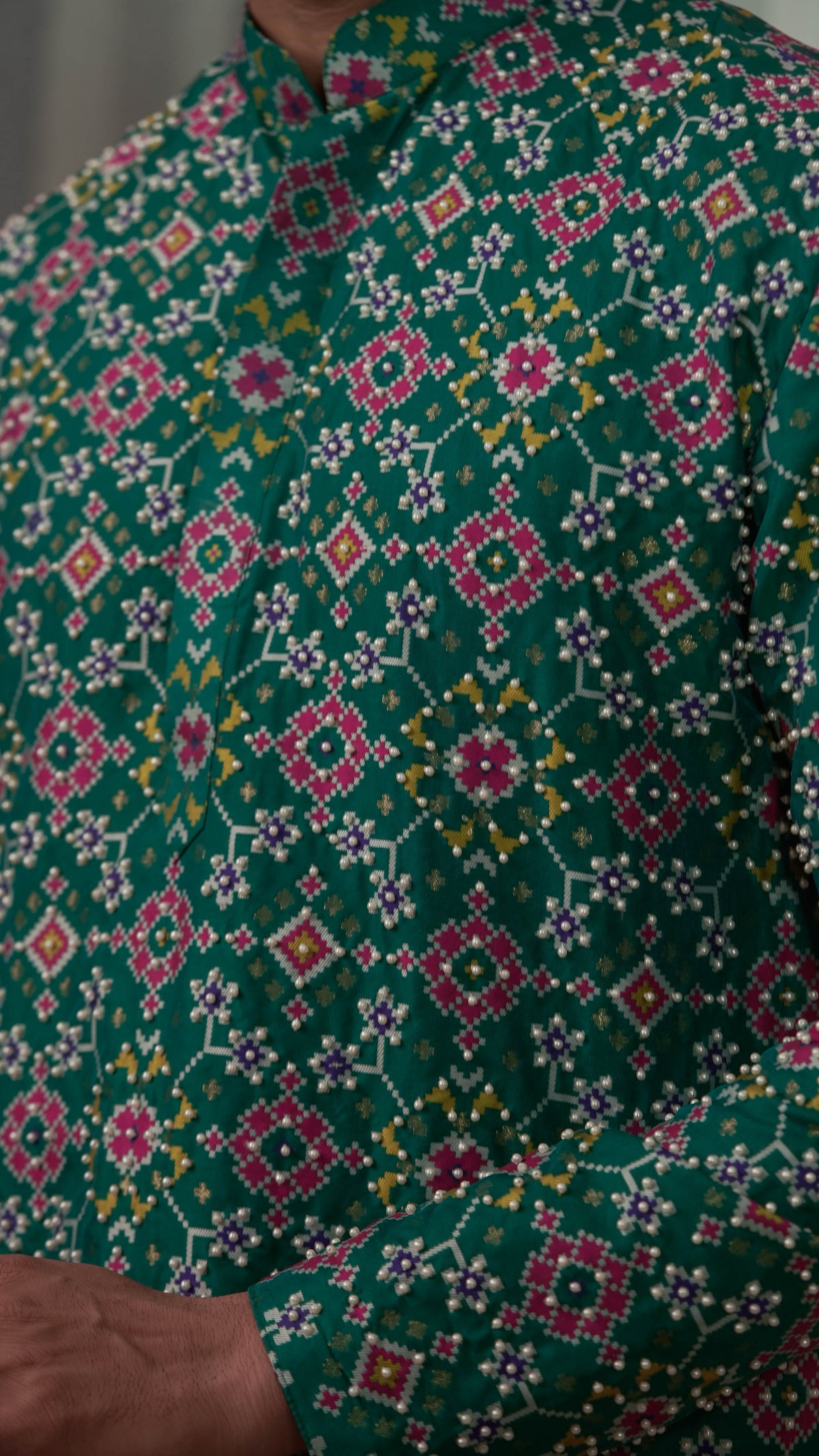 A close-up of a green hand embroidered kurta with a colorful geometric and floral pattern in pink, white, yellow, and orange.