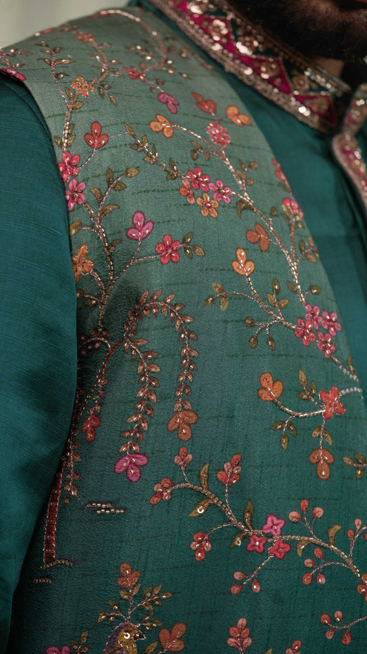 Close-up of a teal green embroidered fabric garment with floral embroidery in pink, orange, and gold tones.