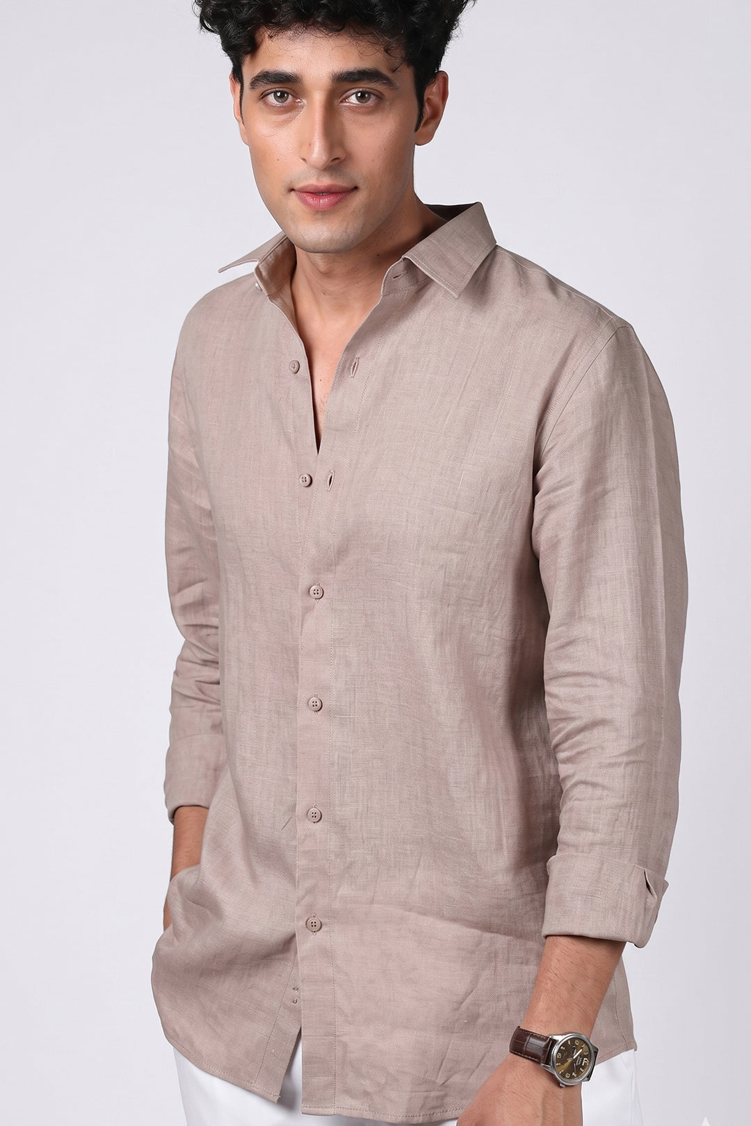 Greige pure linen shirt for men, three-quarter angle view with collar open and sleeves rolled, spread collar and chest pocket detail, styled with white trousers, by BWO