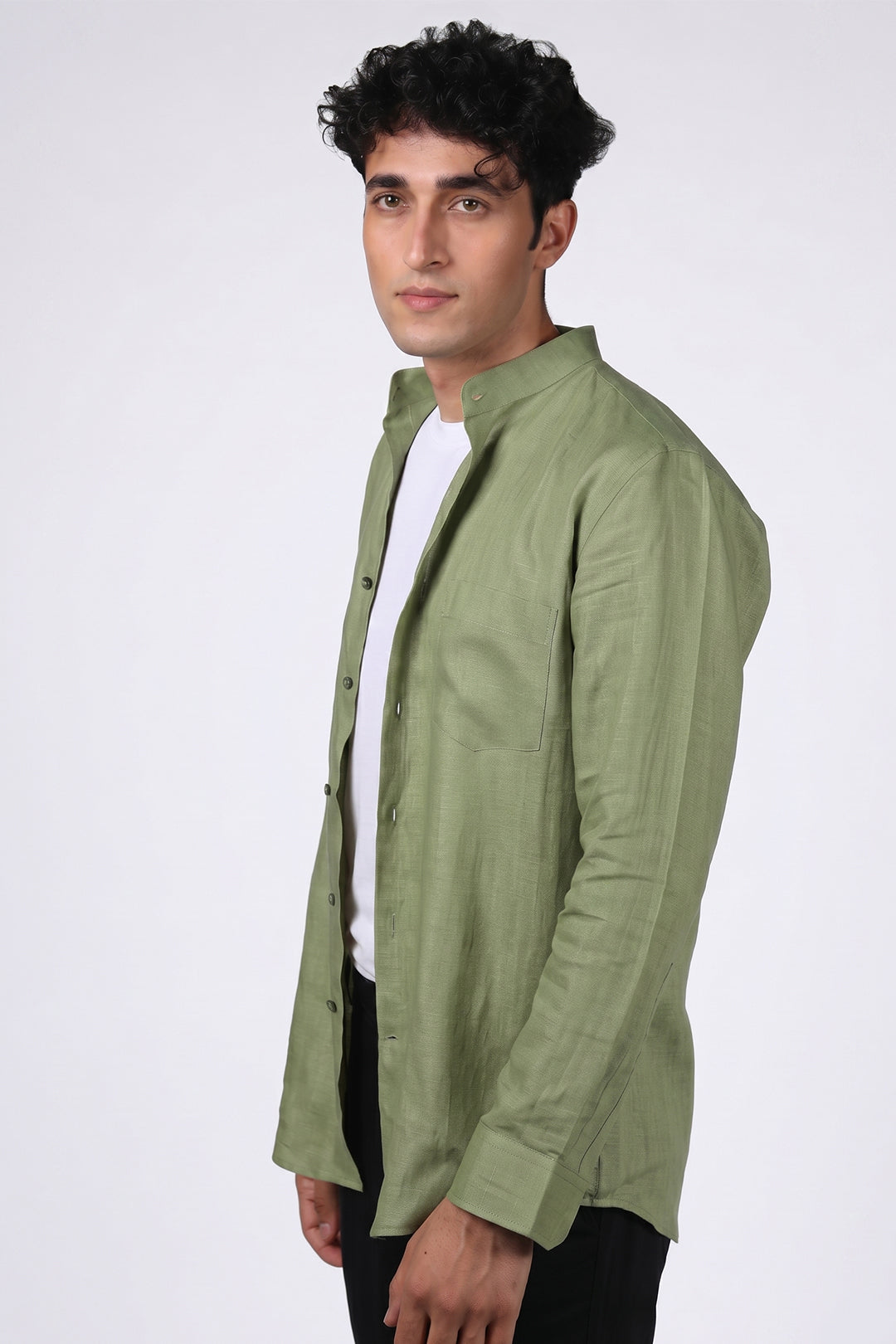 Sage green pure linen shirt for men, three-quarter angle view worn open over white tee, band collar, chest pocket and full button placket visible, styled with black trousers, by BWO