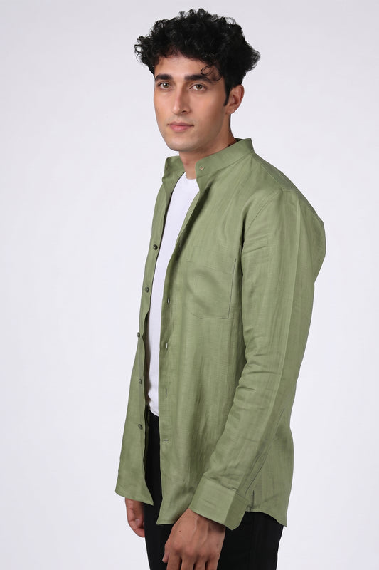 Sage green pure linen shirt for men, three-quarter angle view worn open over white tee, band collar, chest pocket and full button placket visible, styled with black trousers, by BWO