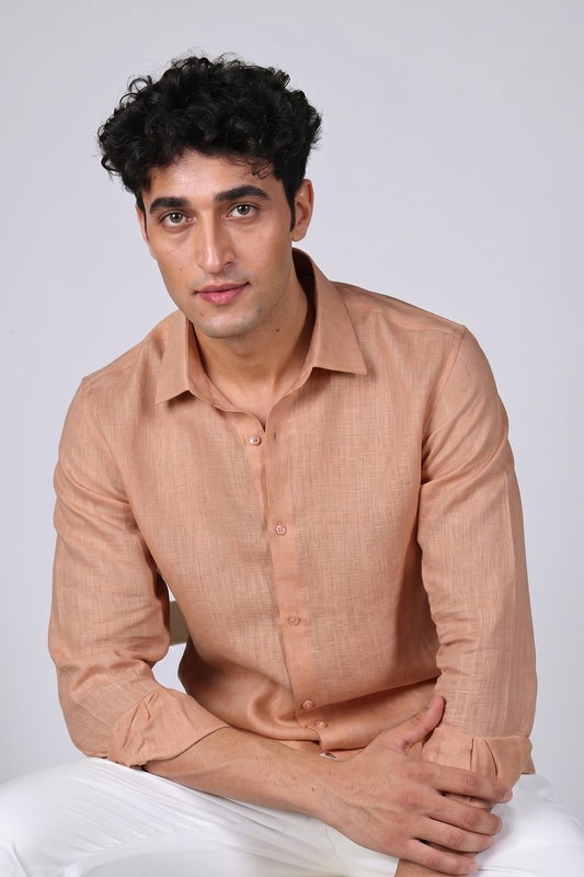 Peach Sandstone pure linen shirt for men, seated portrait with arms crossed, classic spread collar and buttoned cuffs showing linen texture, styled with white trousers, by BWO