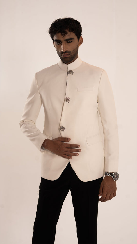 A man modeling a cream-colored traditional Indian jacket (bandhgala) with silver decorative buttons, paired with black trousers, against a plain off-white background.