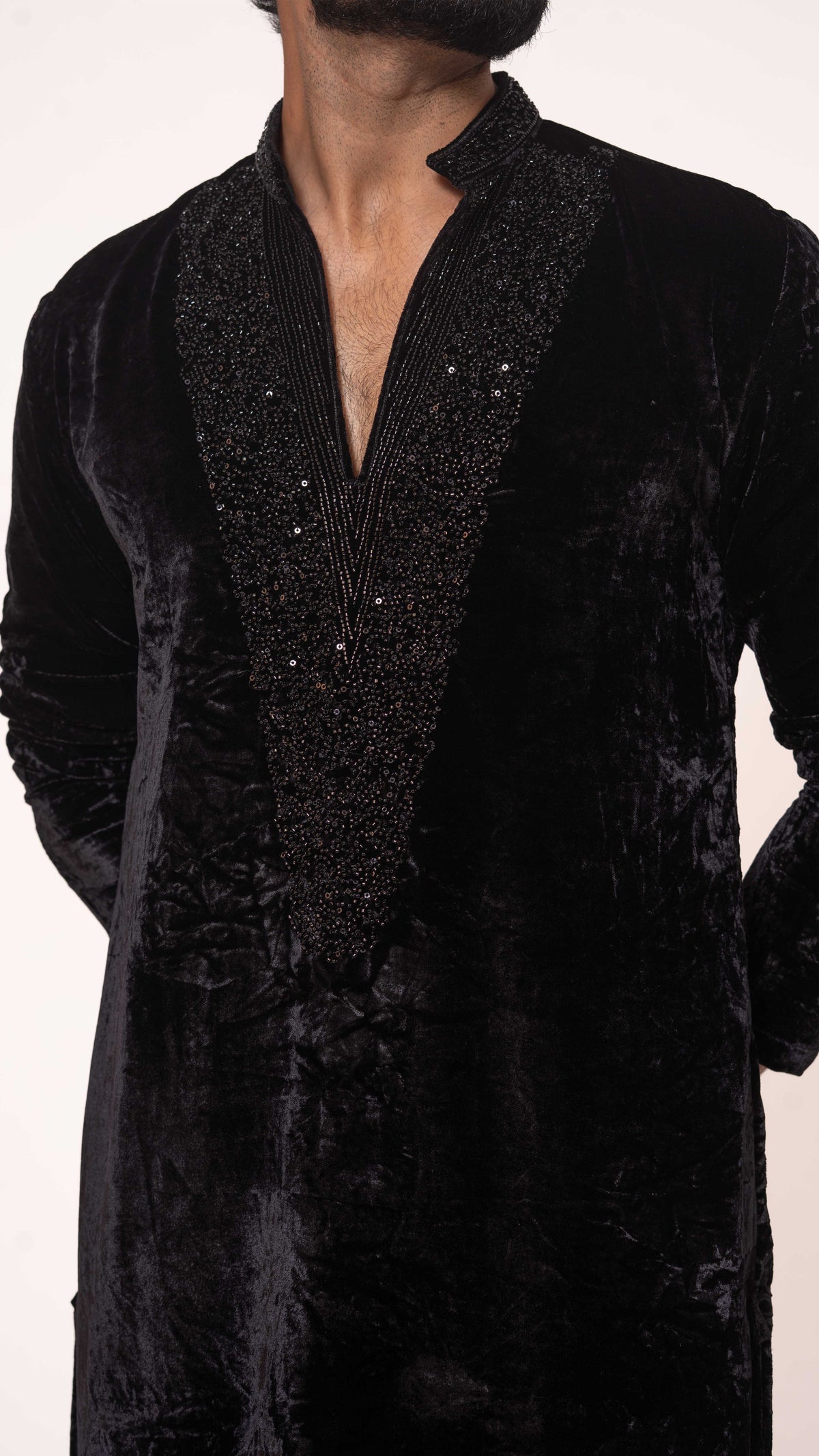 A close-up of a man wearing a black velvet kurta with a heavily embellished black brocade V-neck panel and small silver bead accents.