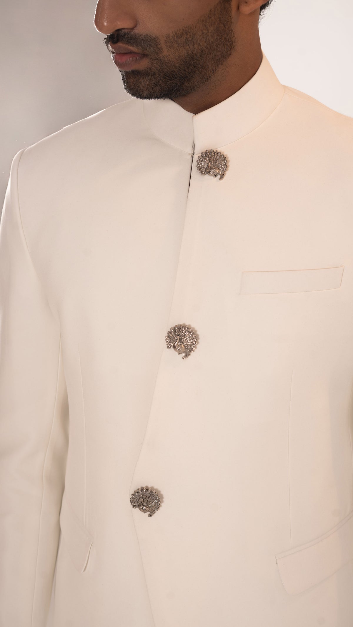 Close-up of a man wearing a cream-colored traditional Indian jacket (sharara) with three ornate metallic decorative buttons.