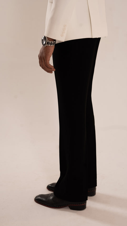 A person shown from the waist down wearing black wide-leg trousers, a cream blazer, and black leather shoes against a plain beige studio background.