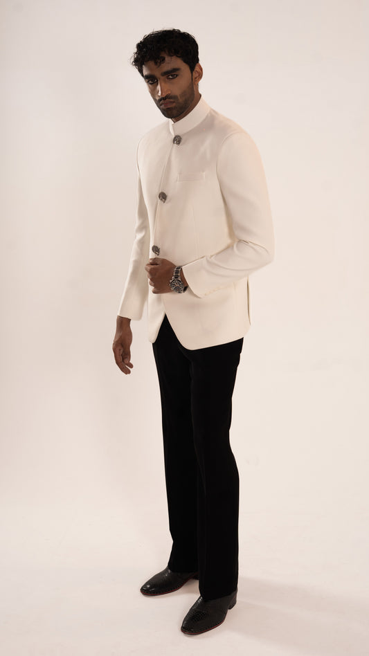 A man modeling a traditional white Indian jacket (jodhpuri) with black trousers and black shoes, standing against a plain off-white studio background.